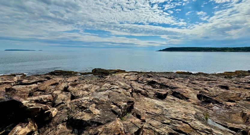 A rocky shore lies before a blue body of water. 